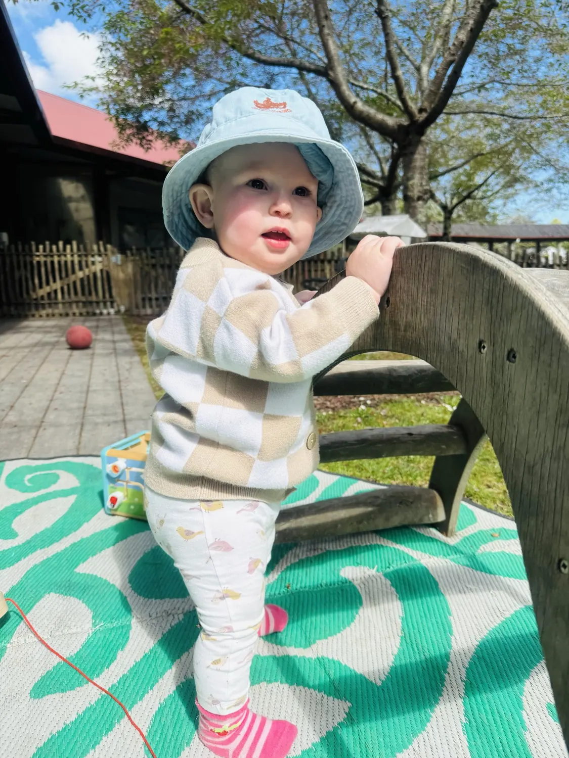 A baby in a sun hat standing up at a wooden climbing arch
