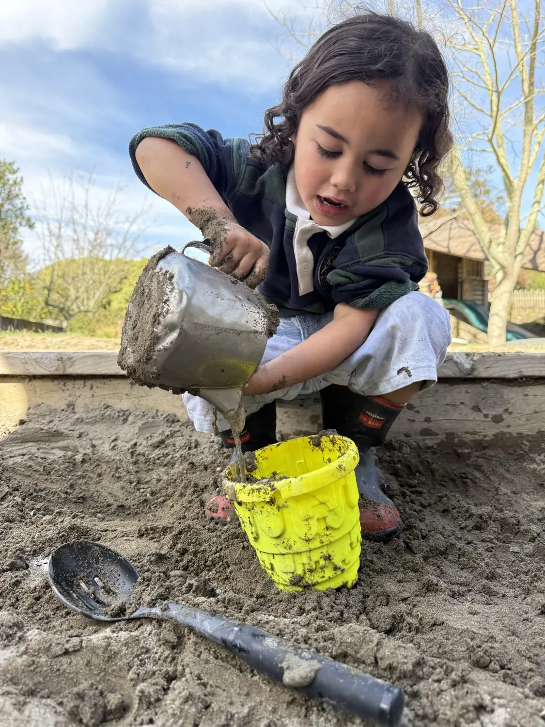 A child pouring mud into a bucket in the sandpit