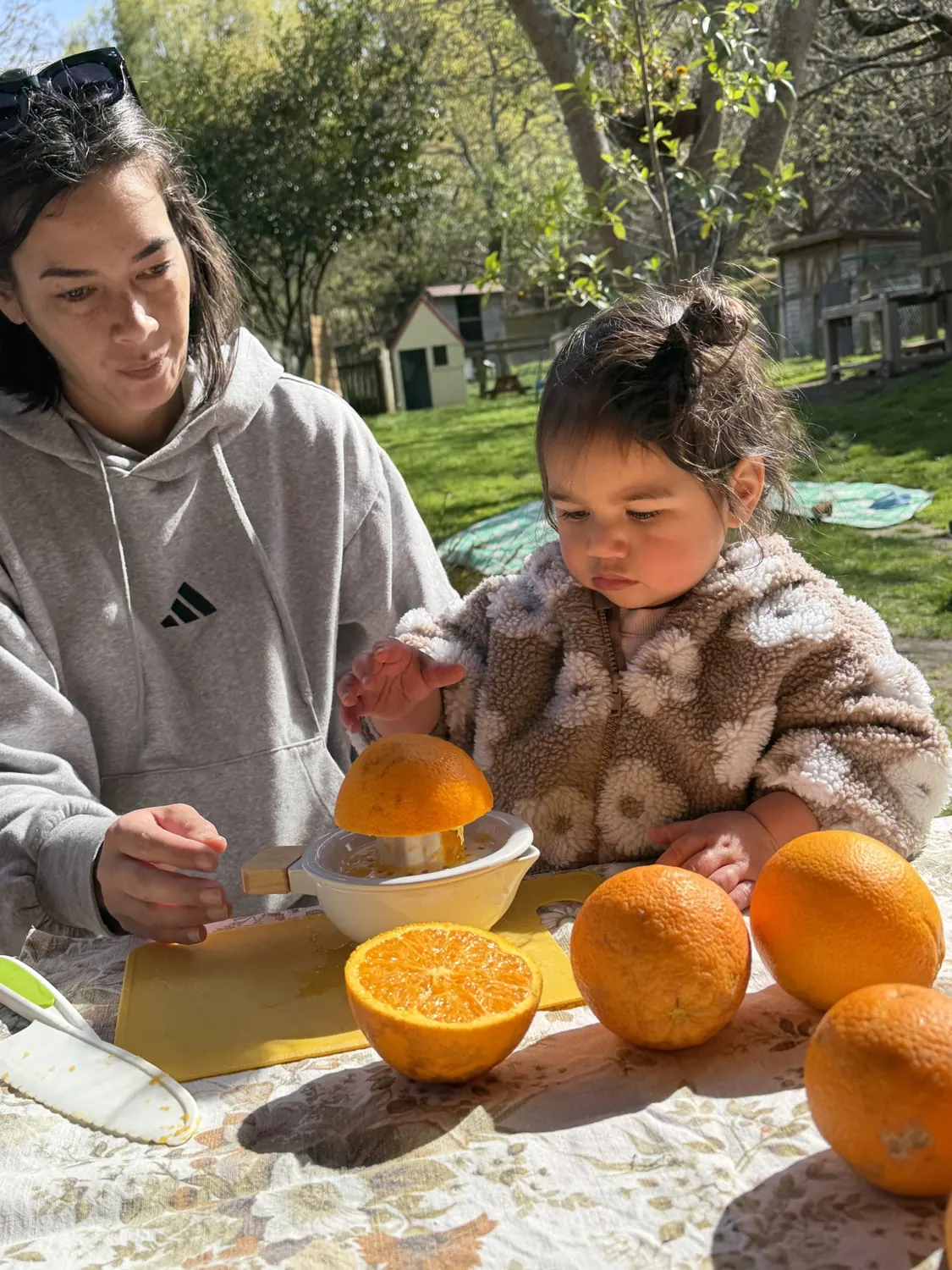 A teacher and a child juicing oranges together at an outdoor table