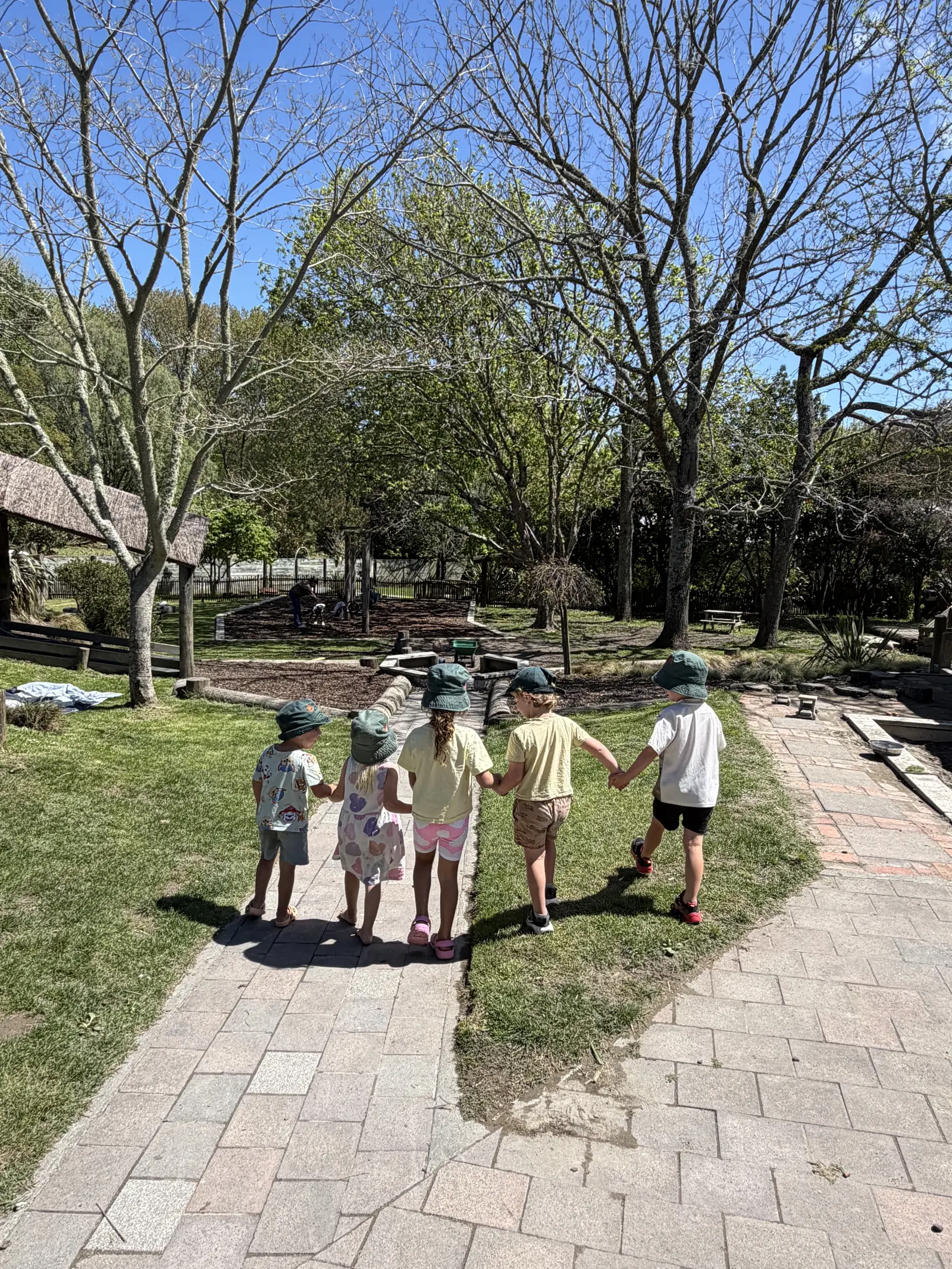 Five children holding hands as they walk along the path through the playground at The Farmyard