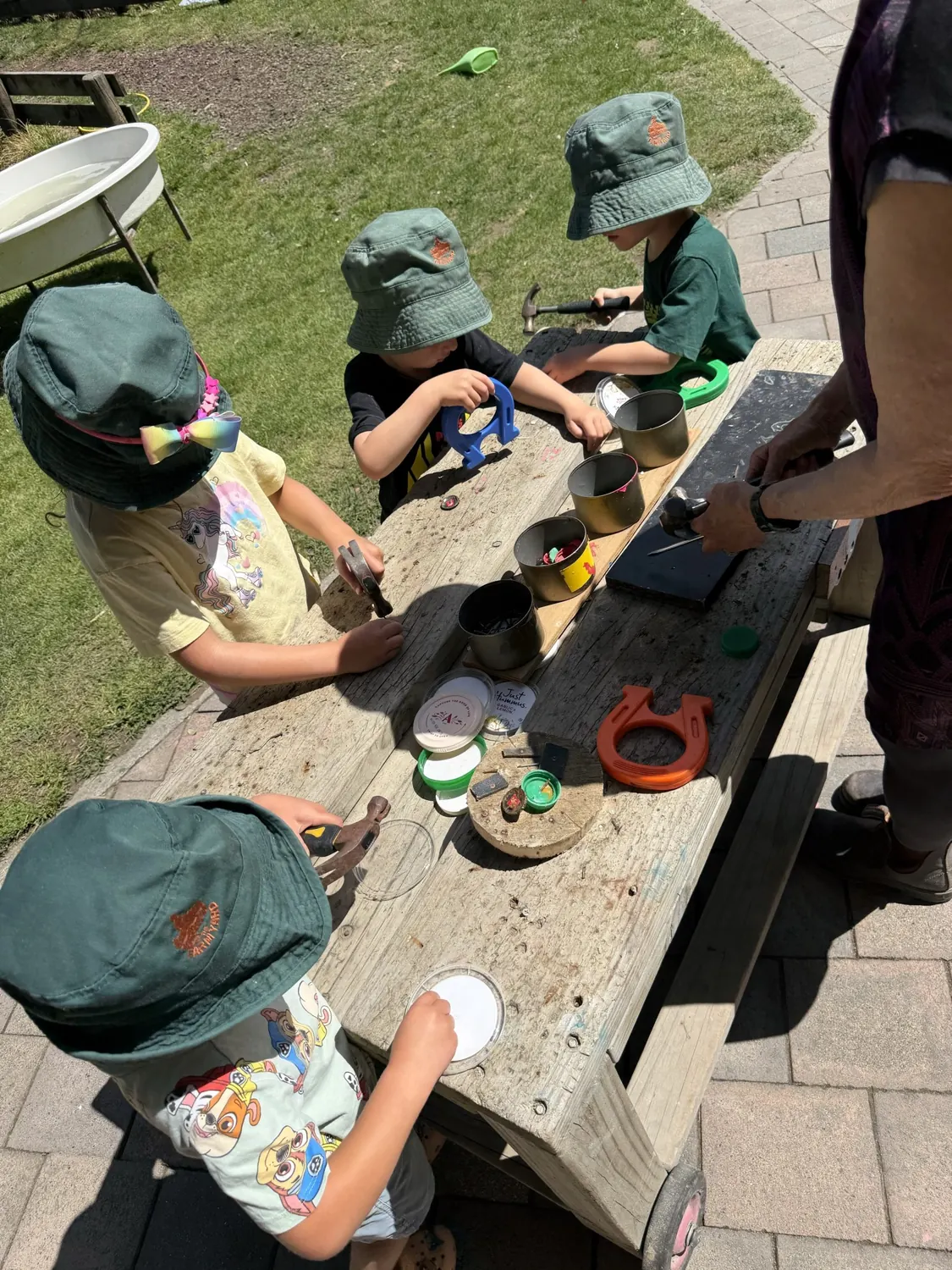 Children in sun hats hammering at the woodwork table with a teacher