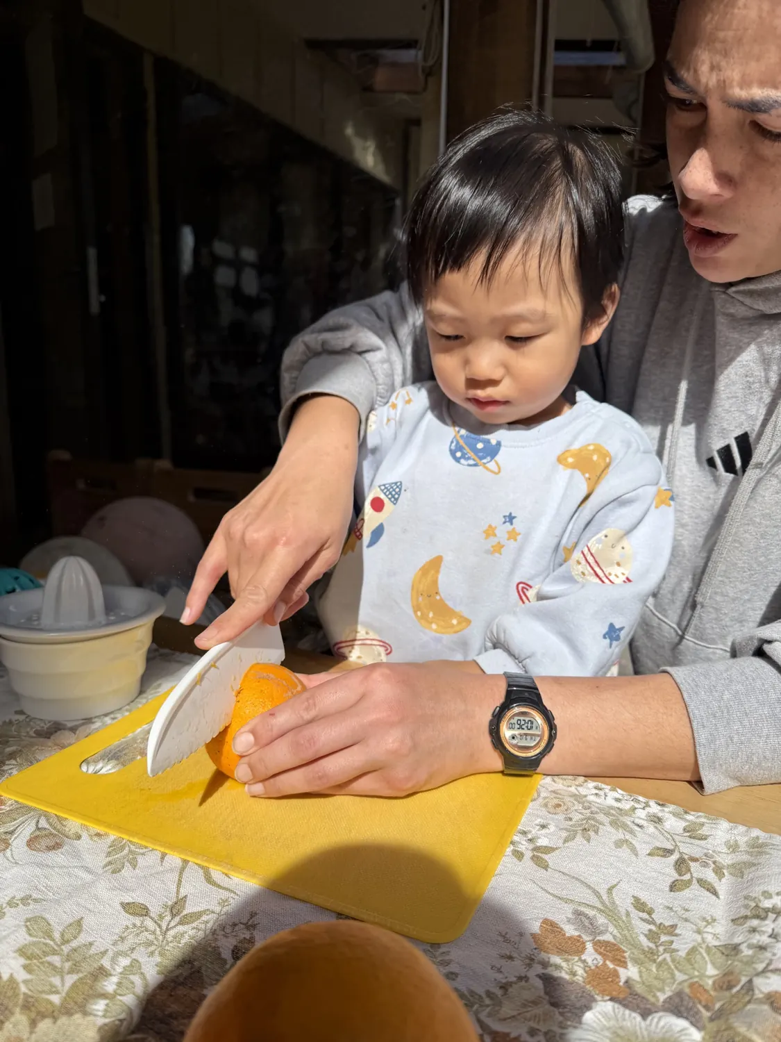 A teacher helping a toddler cut an orange
